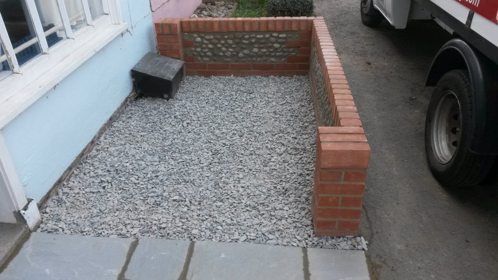 Completed brick-and-flint garden wall beside gravel