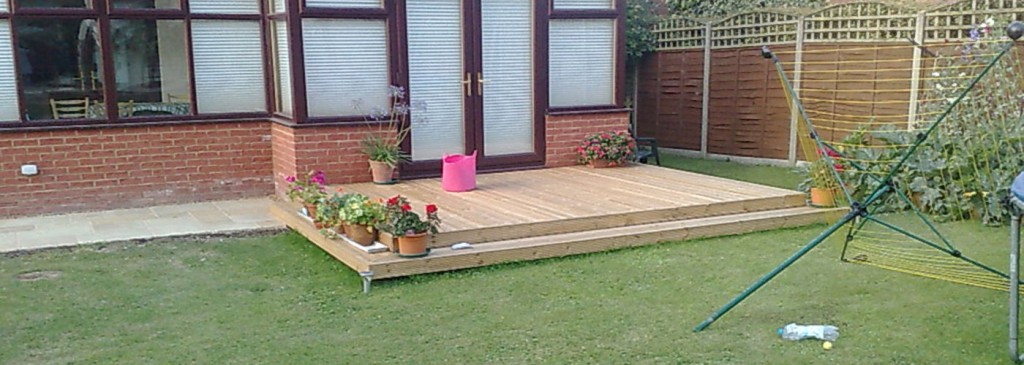Wide view of timber decking beside a brick house and lawn