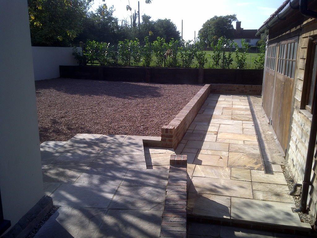 Paved garden terrace beside a raised gravel area and brick wall
