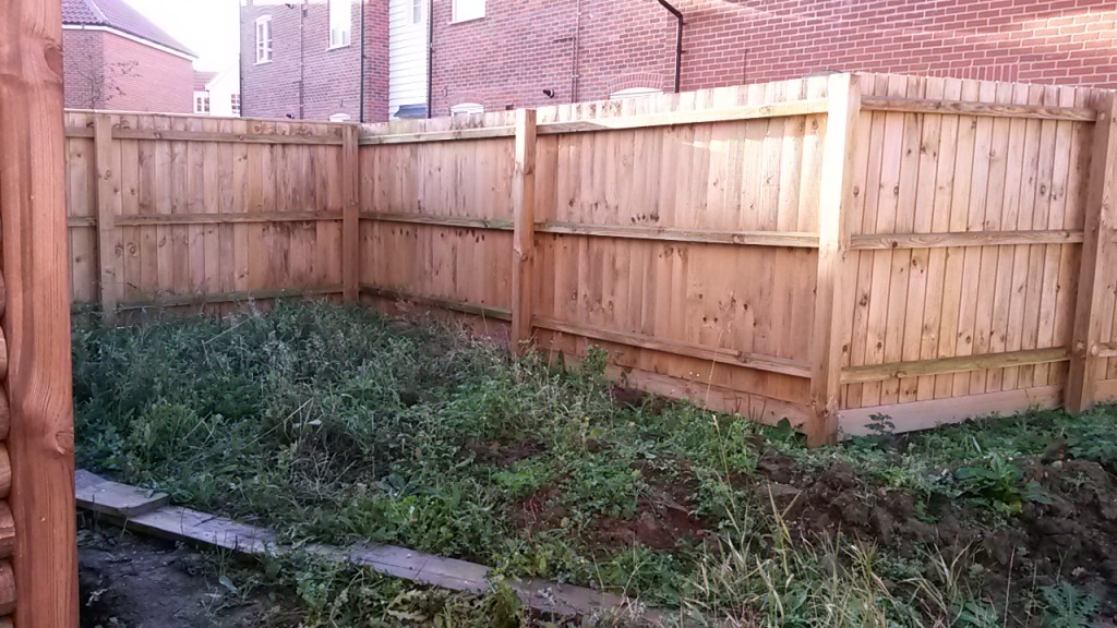 Untidy soil and vegetation beside a timber fence before work