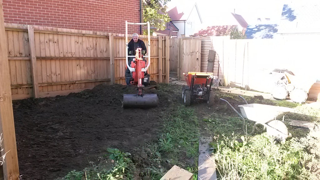 Mini digger beginning clearance in a fenced garden