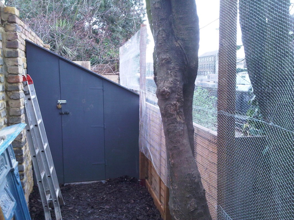 Tall wire mesh fencing beside mature trees and a garden gate