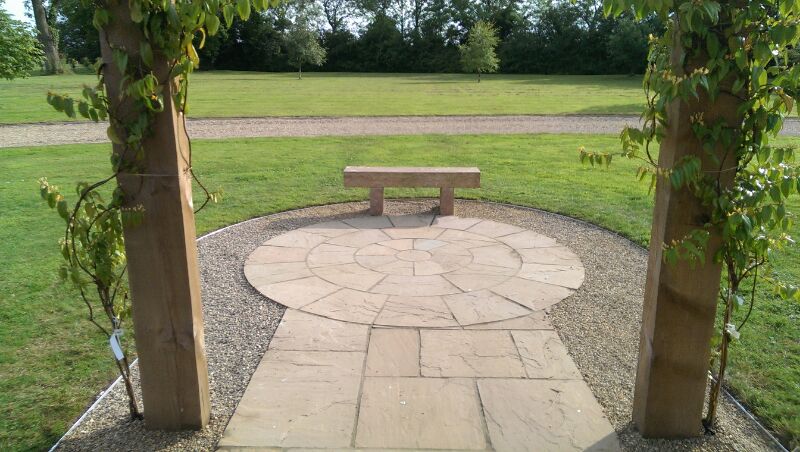 Circular stone patio and bench viewed through a timber pergola