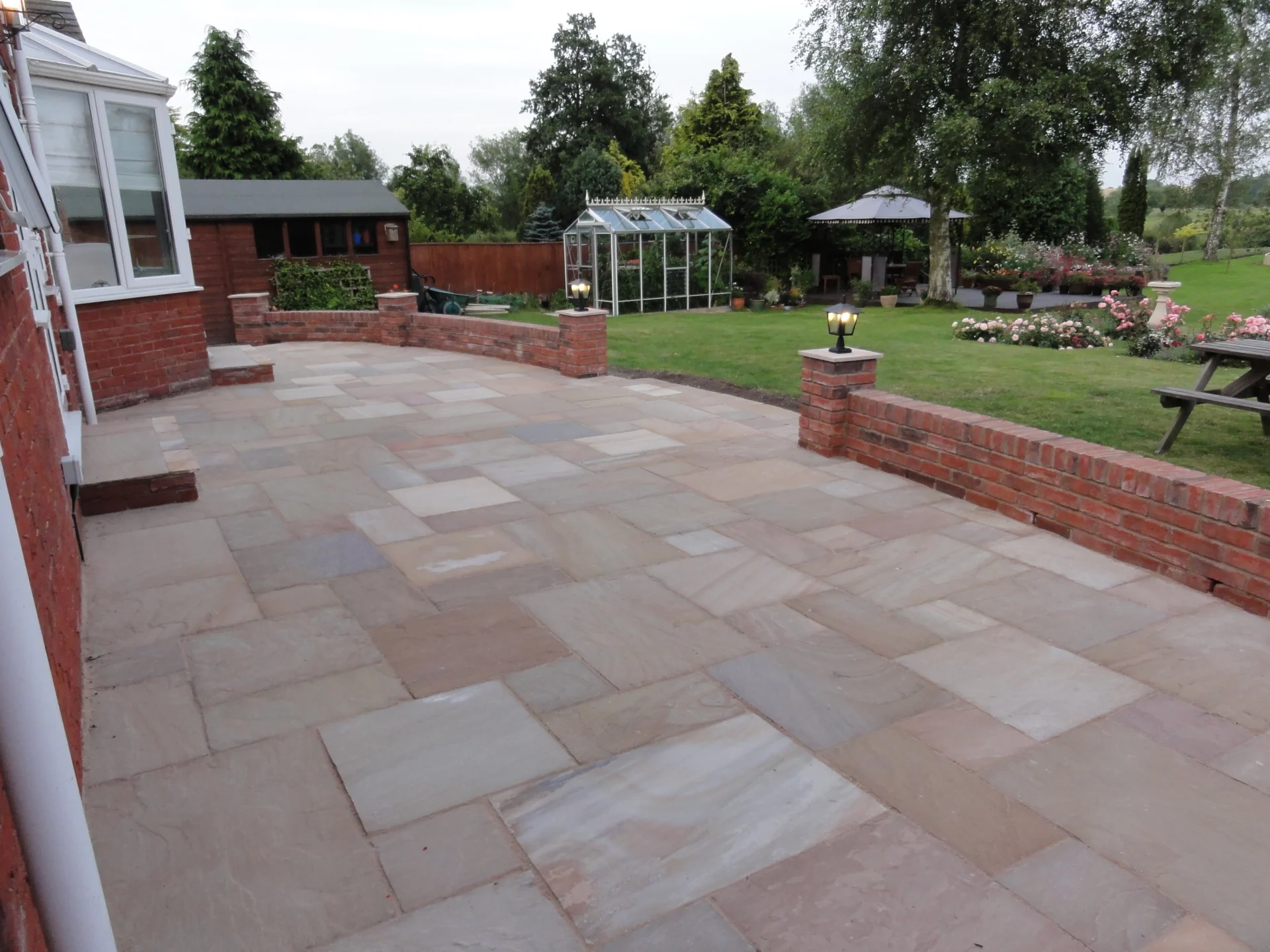 Completed sandstone patio with brick-edged raised borders in Aberdeenshire