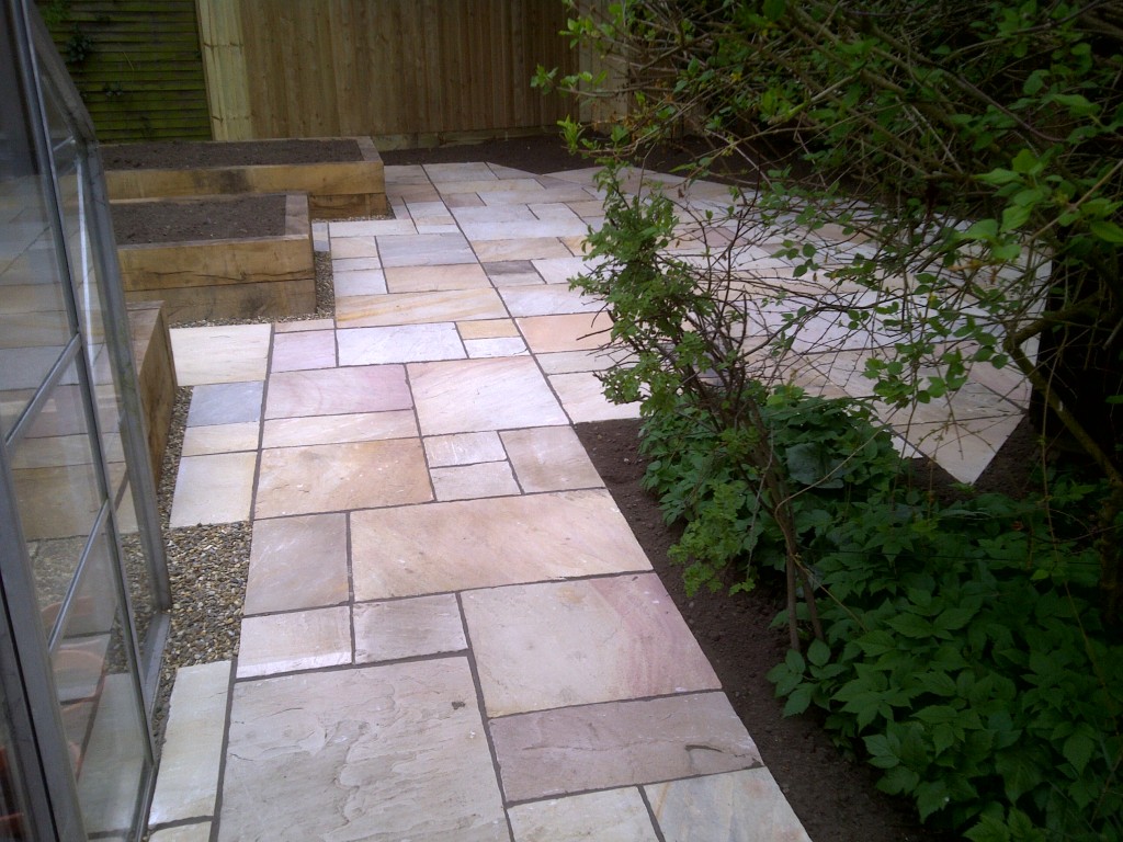 Stone paving beside a greenhouse and timber raised beds