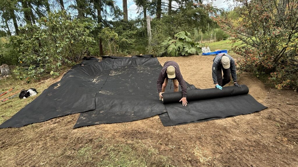 Two team members rolling protective underlay across the prepared pond basin in Aboyne.